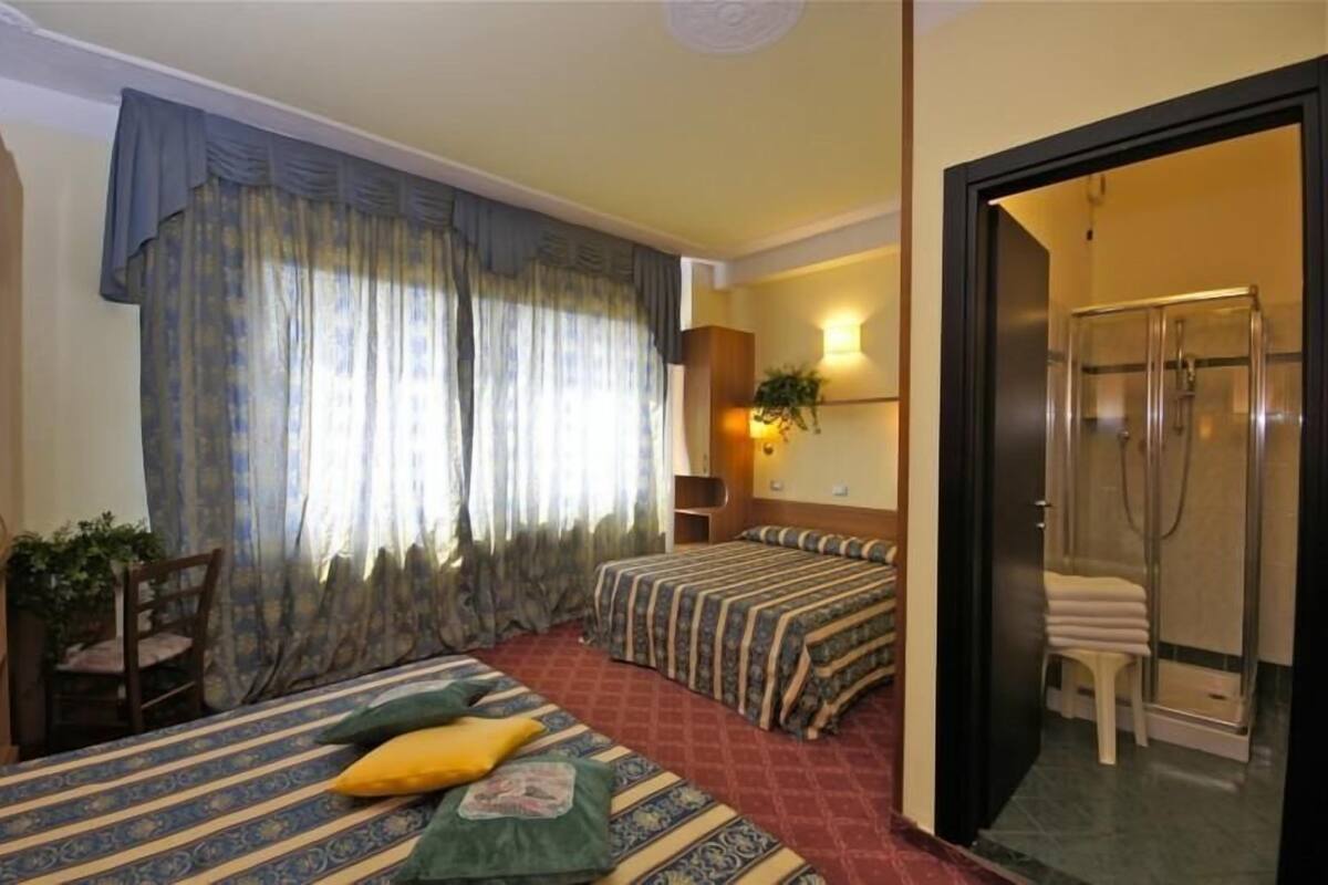 A hotel room with two beds, a shower, a chair, and a plant.