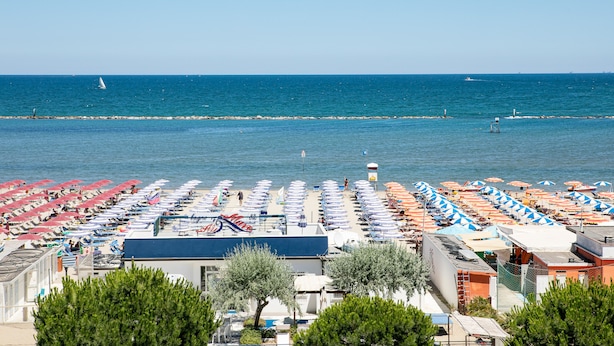 A beachside hotel with rows of sunbeds and umbrellas, a clear view of the sea, and a rocky breakwater in the distance. - Hotel Promenade Universale (Cesenatico)