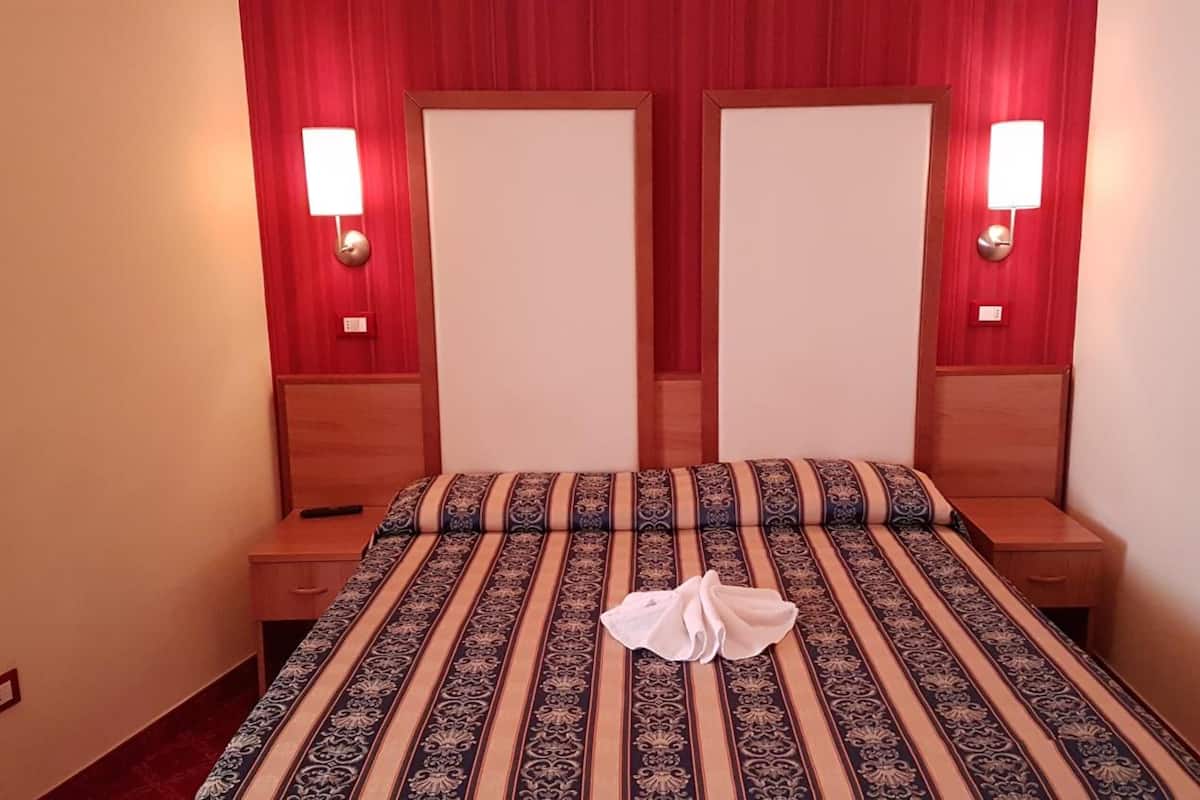A double bed with a patterned bedspread and two nightstands, each with a wall-mounted lamp.