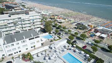 Un hotel con diversi piani, una piscina e una spiaggia attrezzata con ombrelloni e lettini.