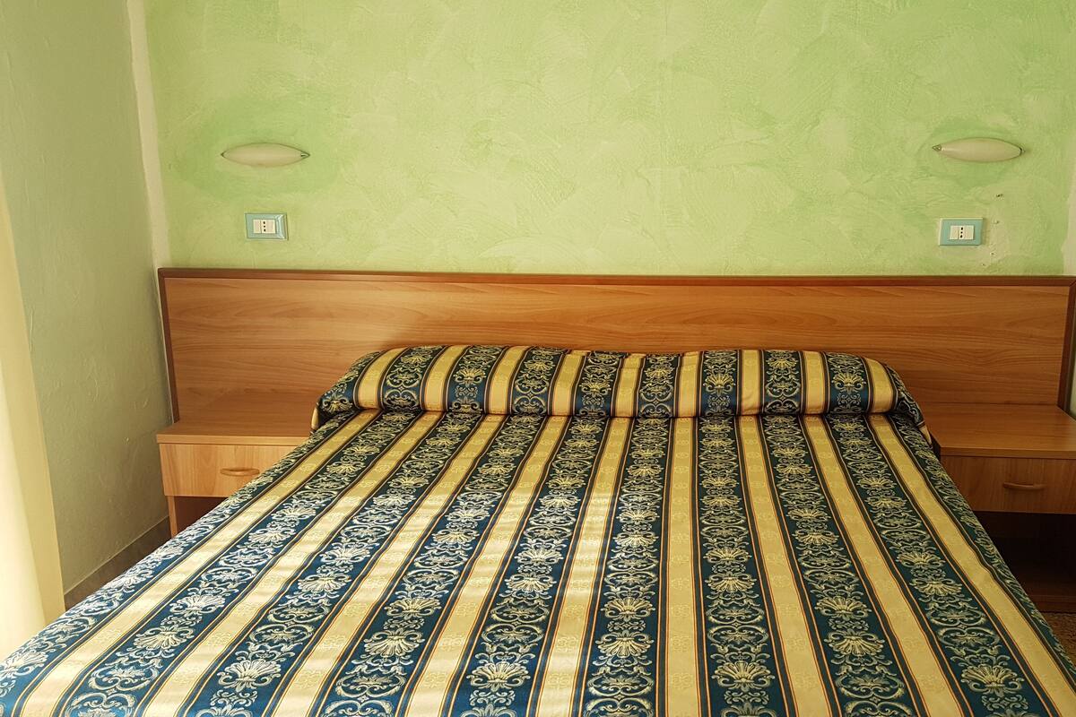 A single bed with a patterned bedspread, wooden headboard, and two bedside tables with light-colored nightstands.