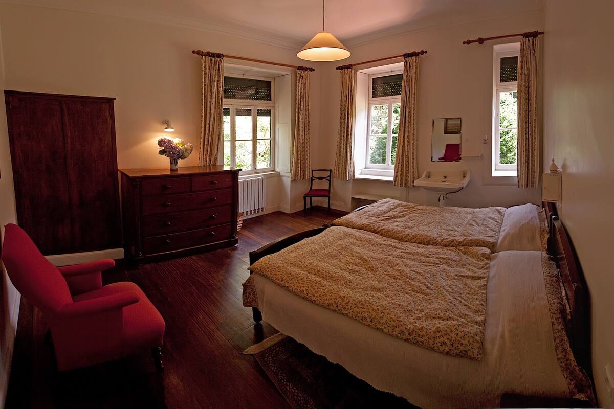 A bedroom with two beds, a dresser, a chair, and a window with curtains.