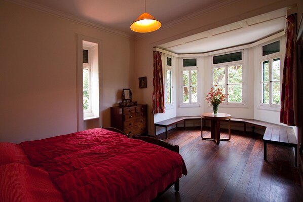 Ein Schlafzimmer mit einem großen Bett, einem Schminktisch, einer Bank und einem Erkerfenster mit Vorhängen.