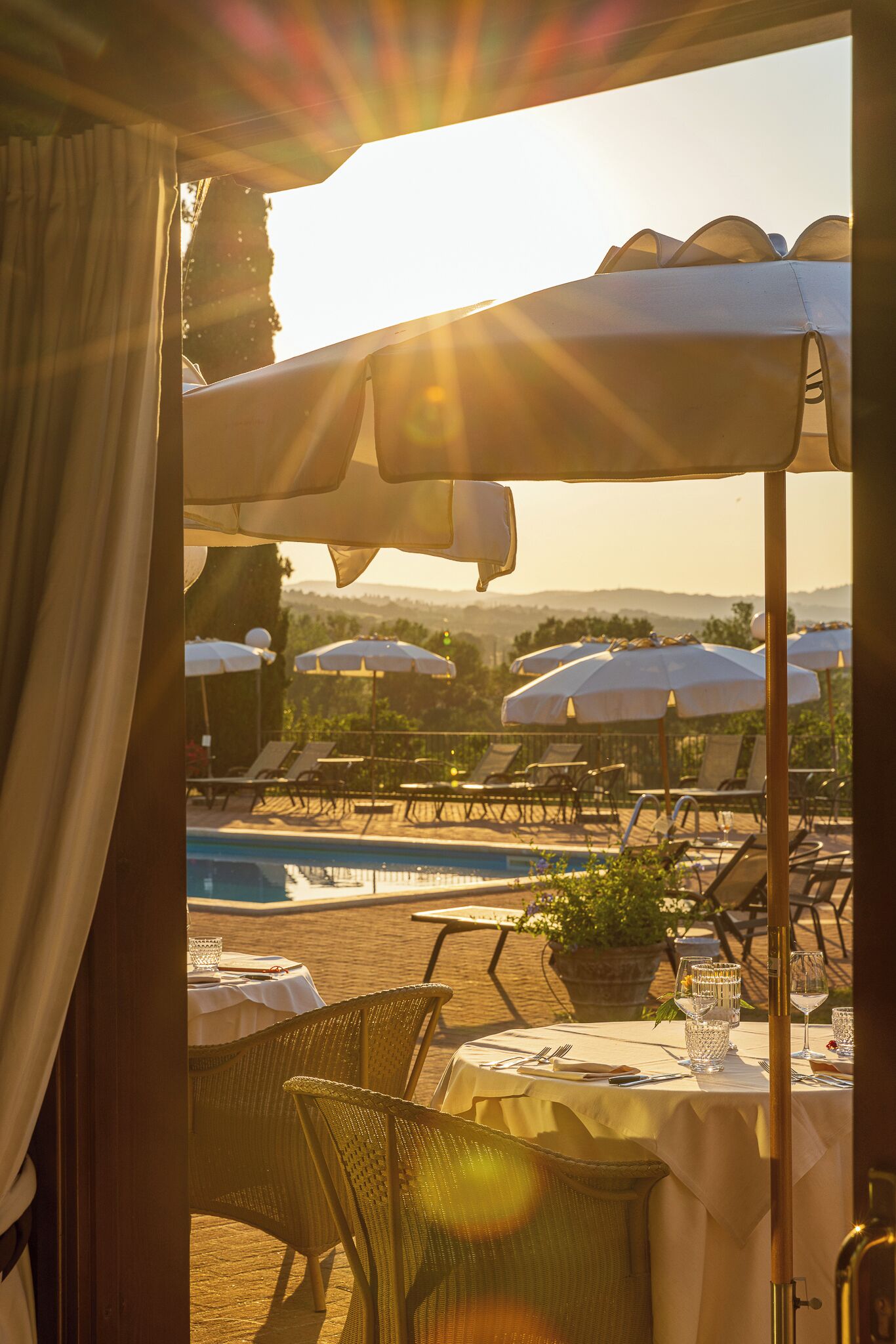 A poolside dining area with umbrellas, lounge chairs, and a table set for two.