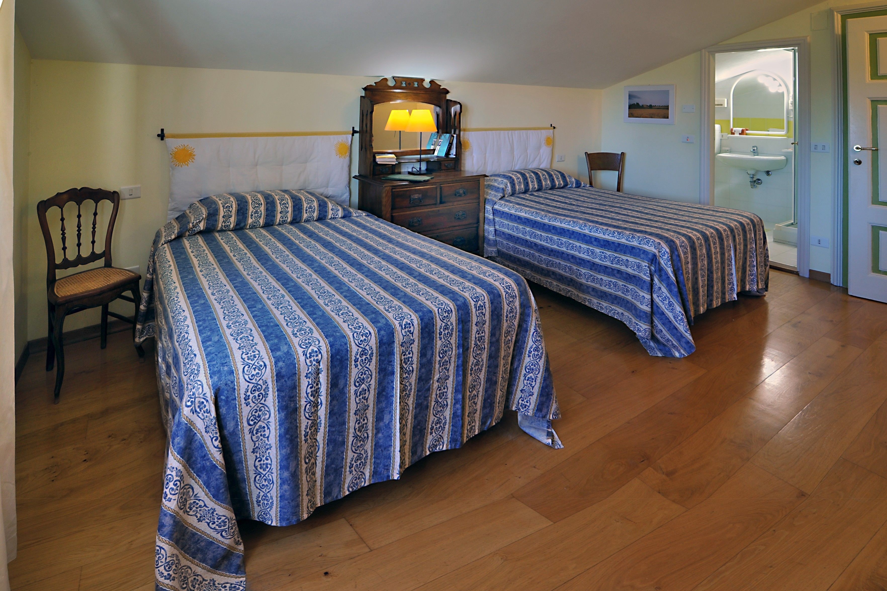A room with two beds, a wooden dresser, a chair, and a bathroom visible through an open door.