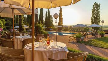 An outdoor dining area with round tables, wicker chairs, and umbrellas.
