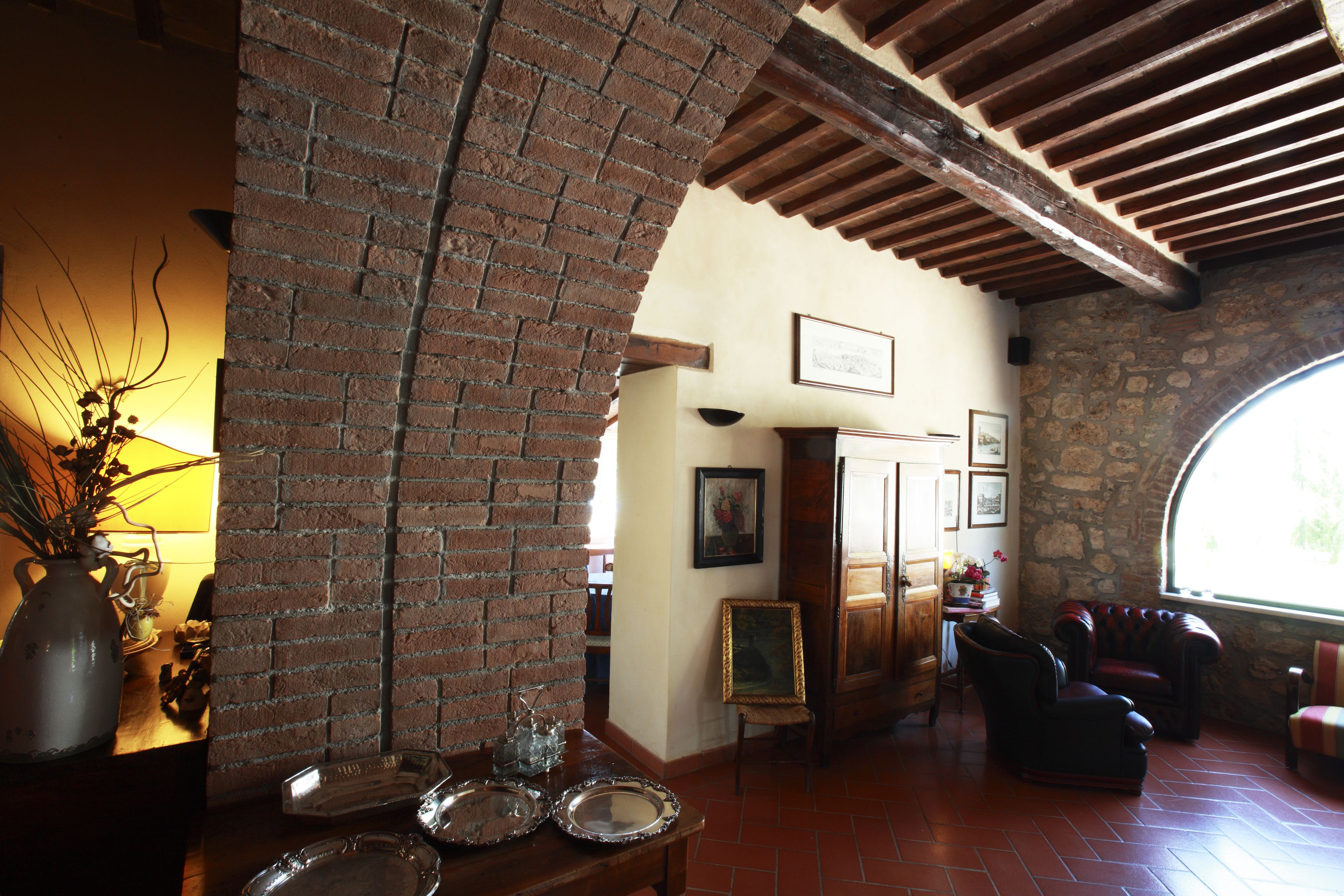 A room with a brick wall, wooden beams, a fireplace, and a large window.