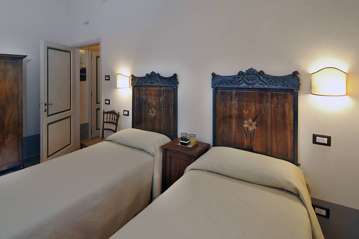 Une chambre d’hôtel avec deux lits simples, des têtes de lit en bois, des lampes de chevet, une table de chevet en bois et une chaise.
