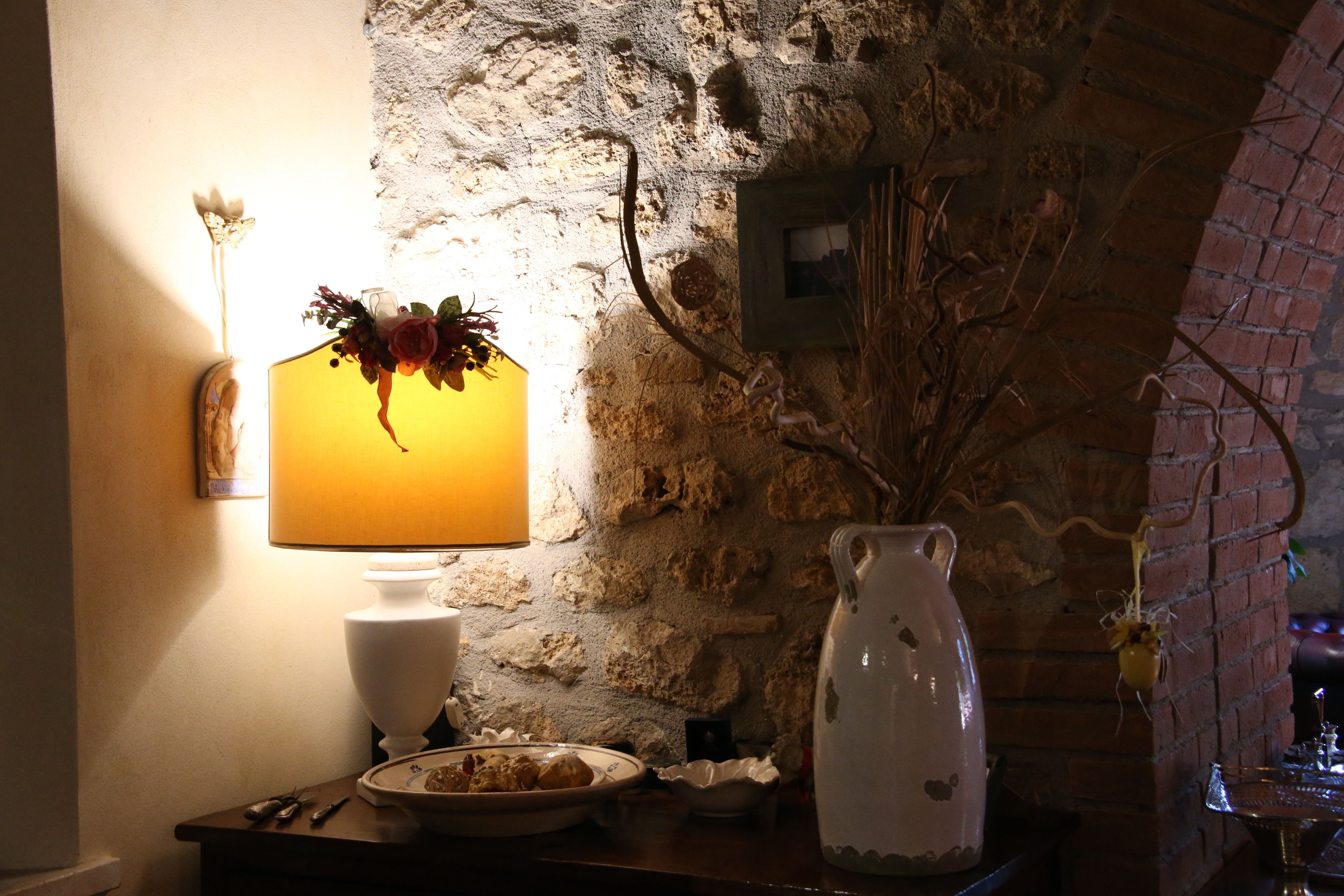 A stone wall with a lamp, a vase, and a plate of cookies on a table.