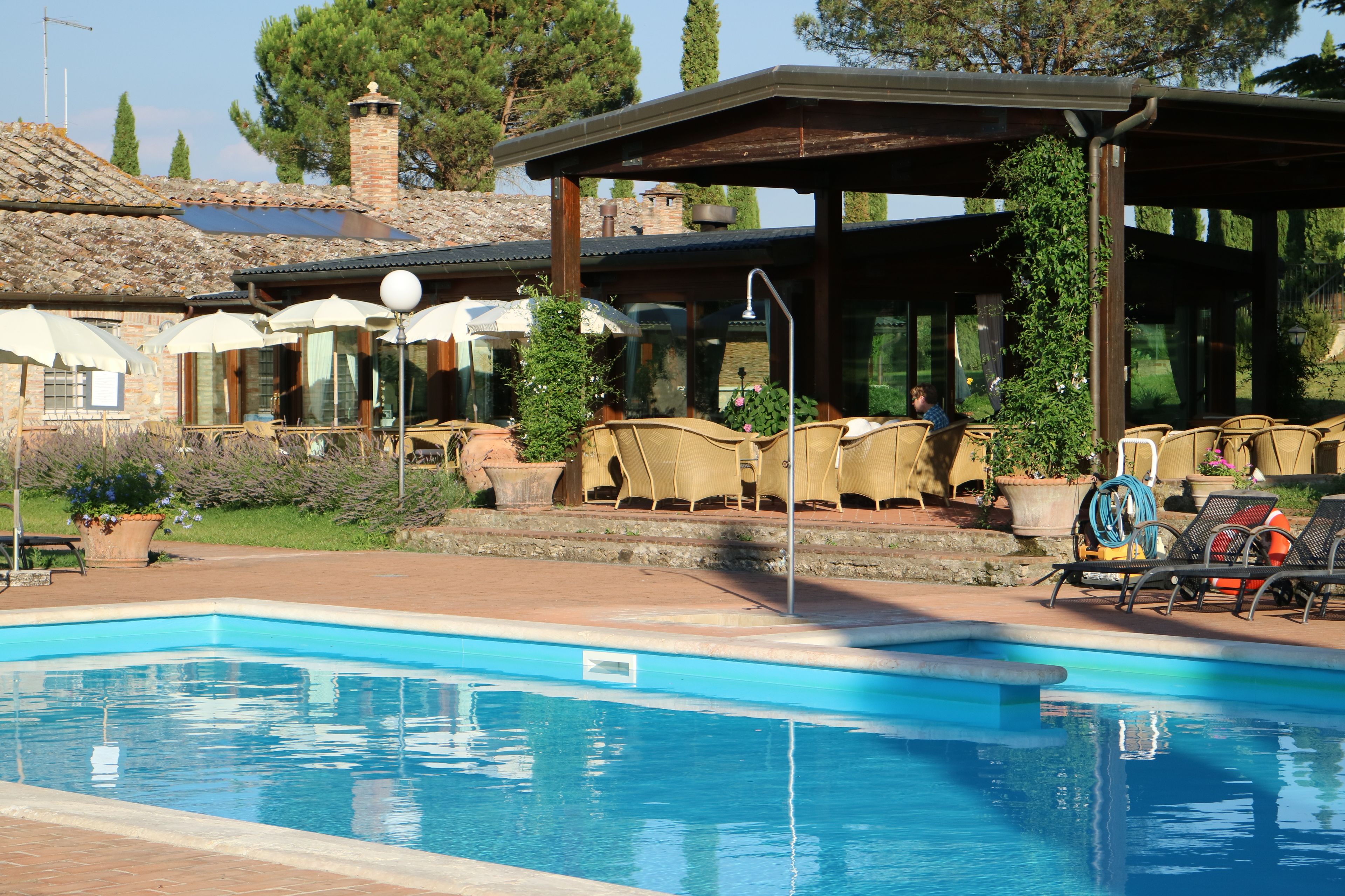 A pool area with lounge chairs and umbrellas, surrounded by a stone building with a tiled roof and a chimney.