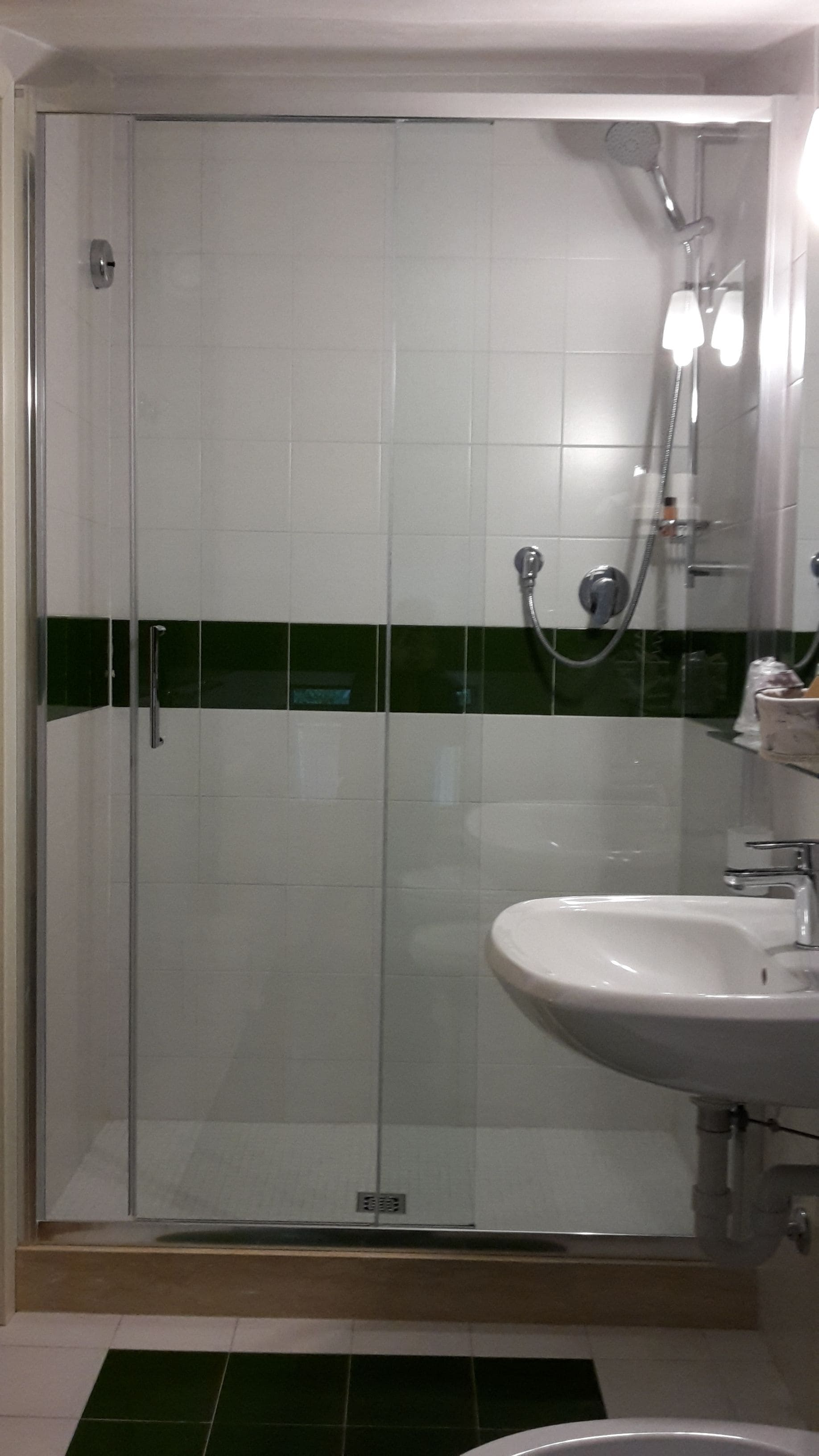 A bathroom with a glass-enclosed shower, a white sink, and a green stripe on the wall.