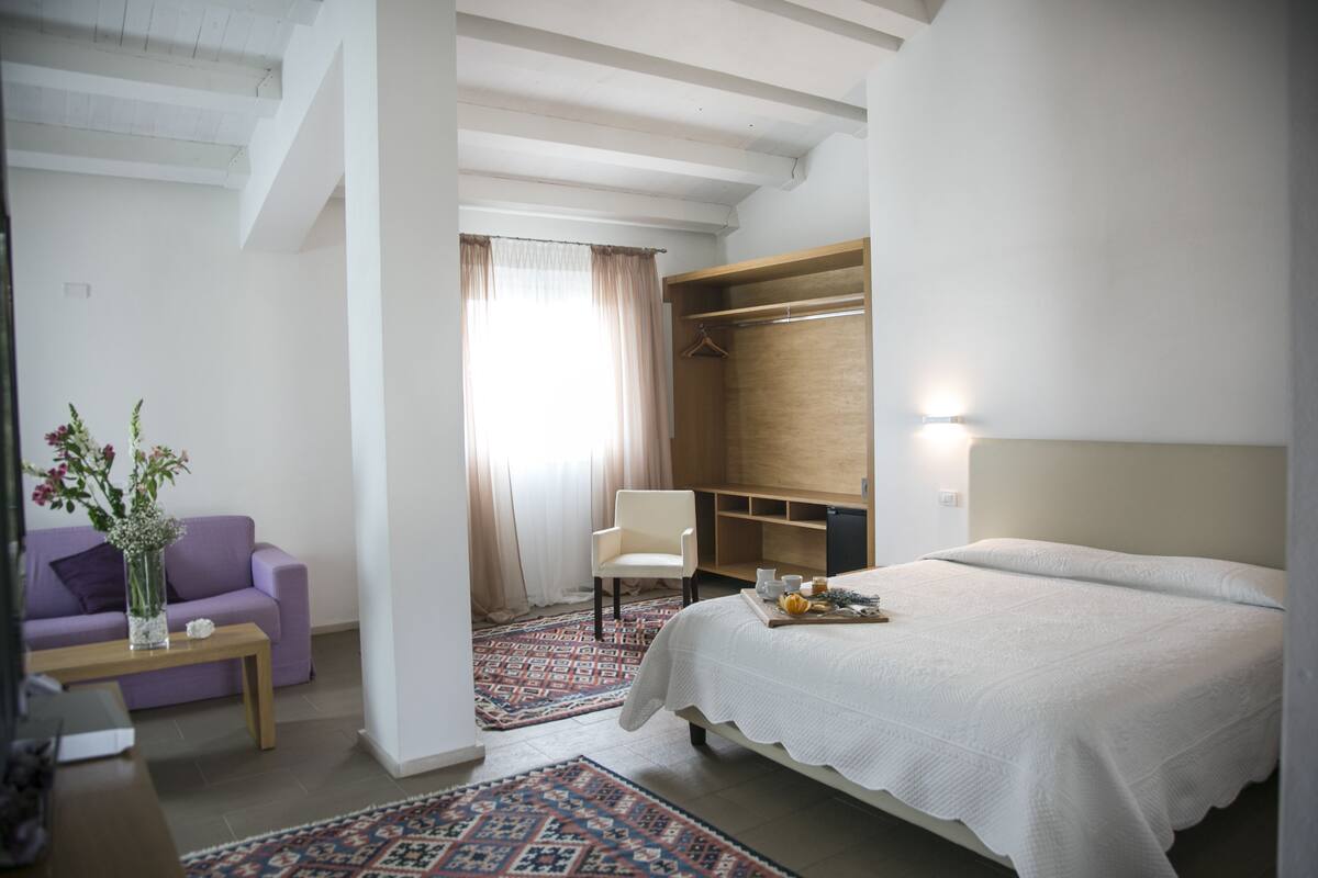 A bedroom with a bed, a chair, a sofa, a desk, and a wardrobe.