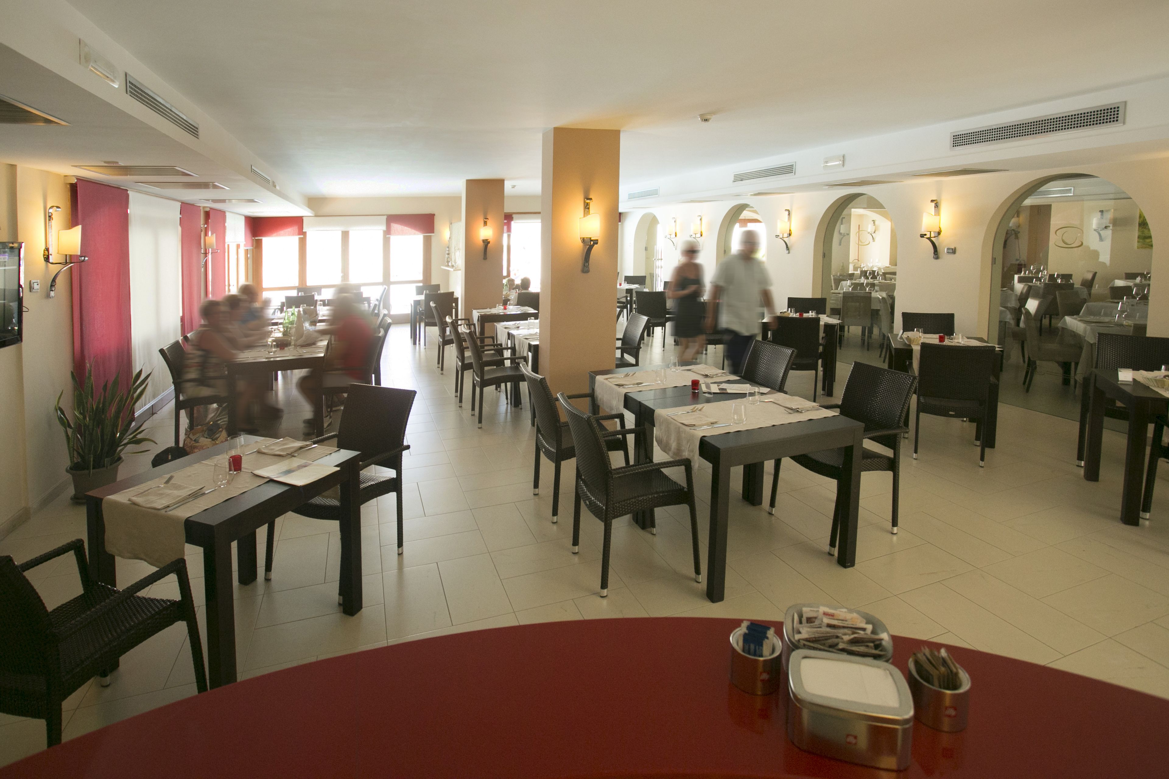 Ein geräumiges Restaurant mit mehreren Tischen und Stühlen, großen Fenstern und einer roten Akzentwand.