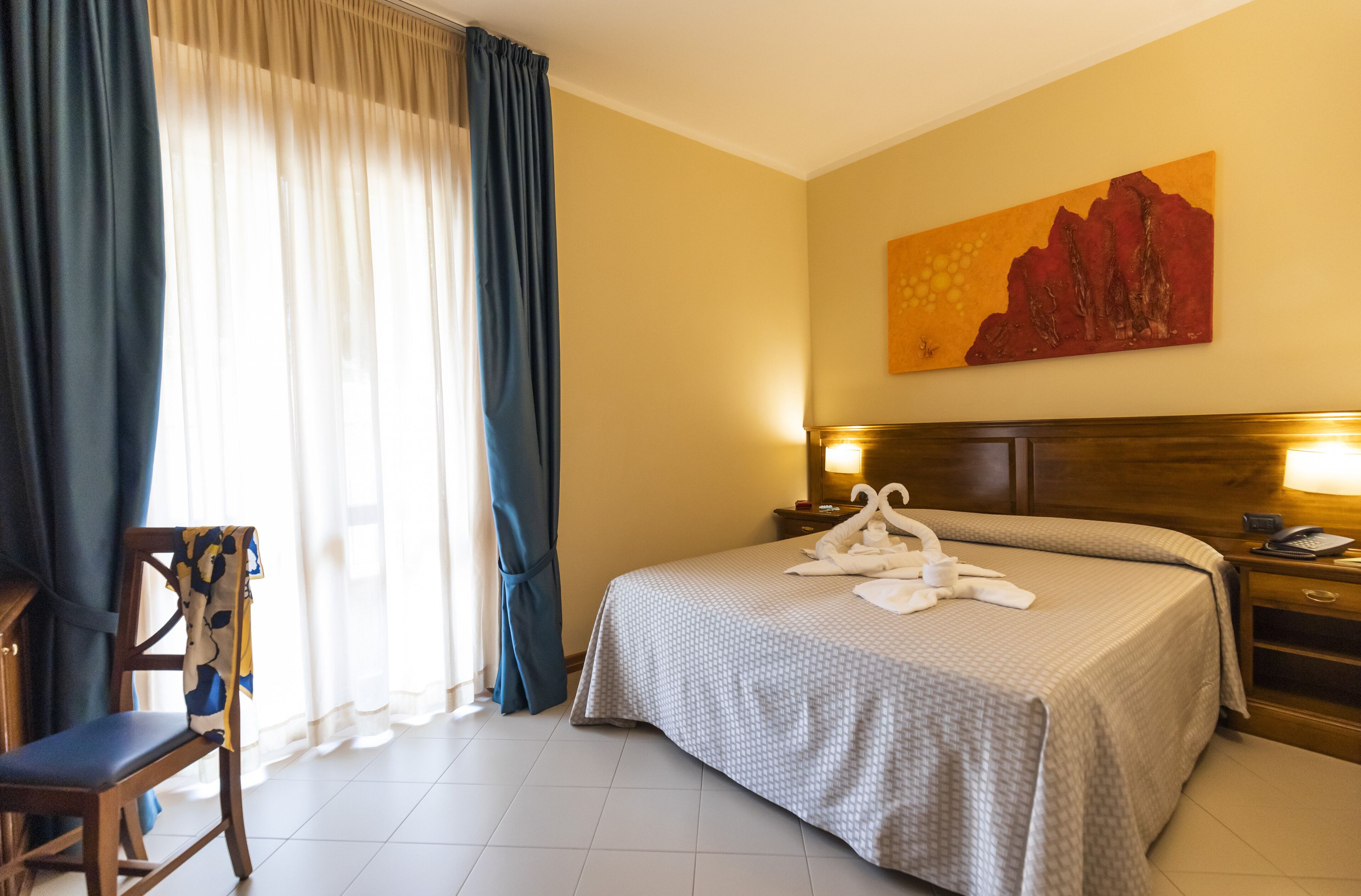 A hotel room with a bed, a chair, a nightstand, and a painting on the wall.