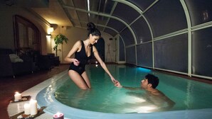 An indoor swimming pool with a glass ceiling, candles, and a tray of snacks.