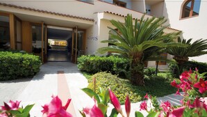 A hotel entrance with a covered walkway, palm trees, and flowering plants.