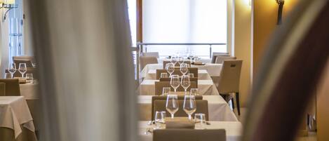 A restaurant with tables set for dining, a large window, and a wall-mounted light fixture.