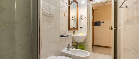 A bathroom with a toilet, bidet, sink, and mirror.