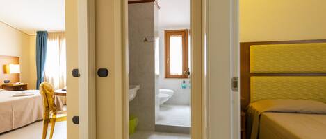 Habitación de hotel con cama, una silla, un escritorio y un baño visible a través de una puerta abierta.