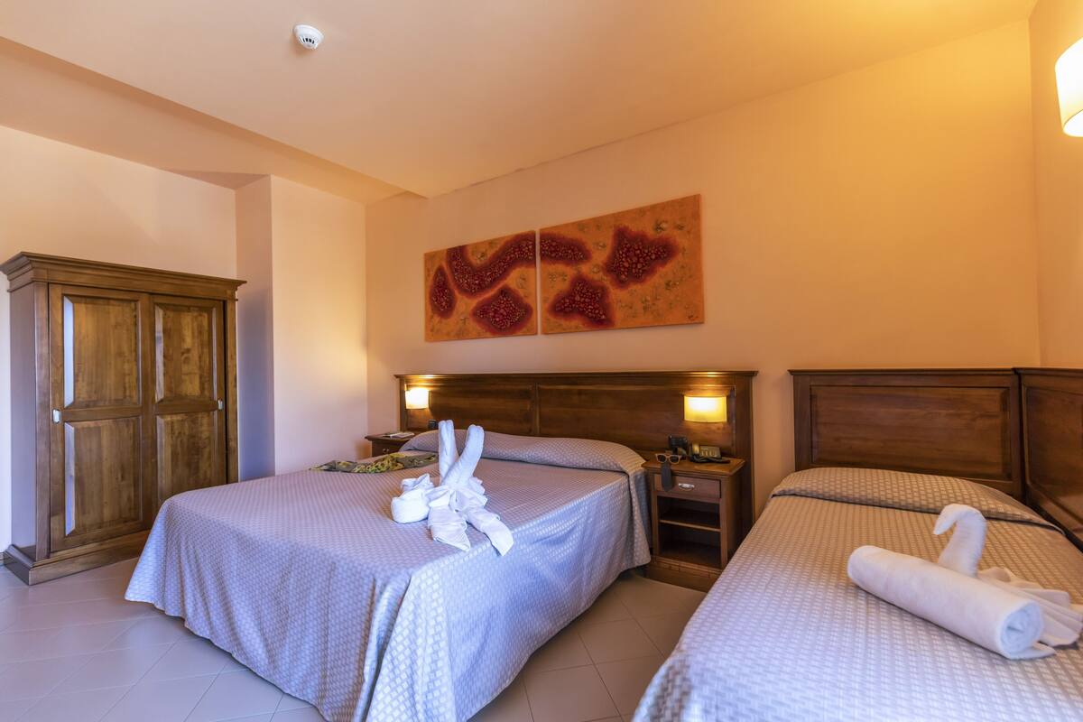 A hotel room with two beds, wooden headboards, bedside tables, and a large painting on the wall.