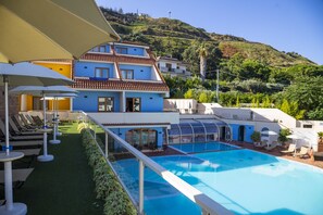 A pool area with sun loungers and umbrellas, a clear blue pool, and a hillside with buildings in the background. - Tropis Hotel (Tropea)