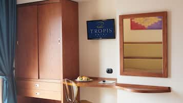 Habitación de hotel con un armario de madera, un escritorio con una bandeja de fruta, una silla, un televisor de pantalla plana y un espejo decorativo.