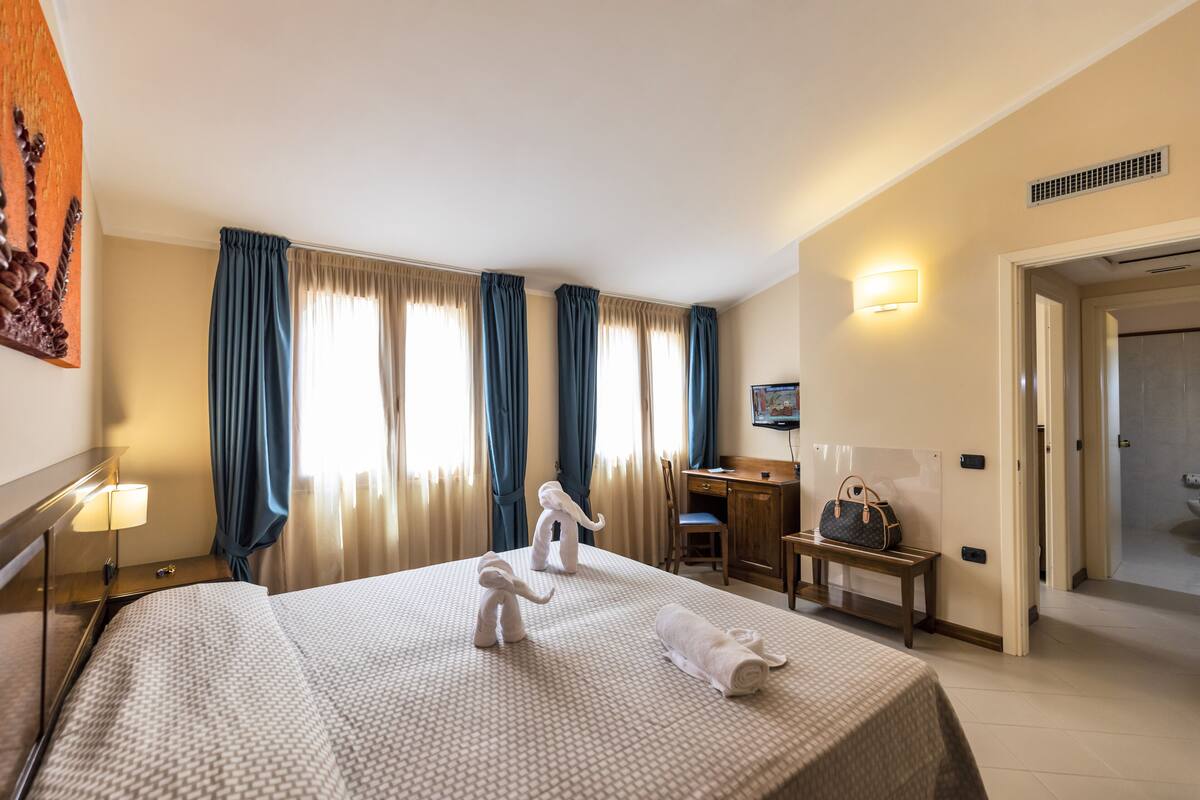 A hotel room with a bed, two nightstands, a desk, a chair, and a bench.