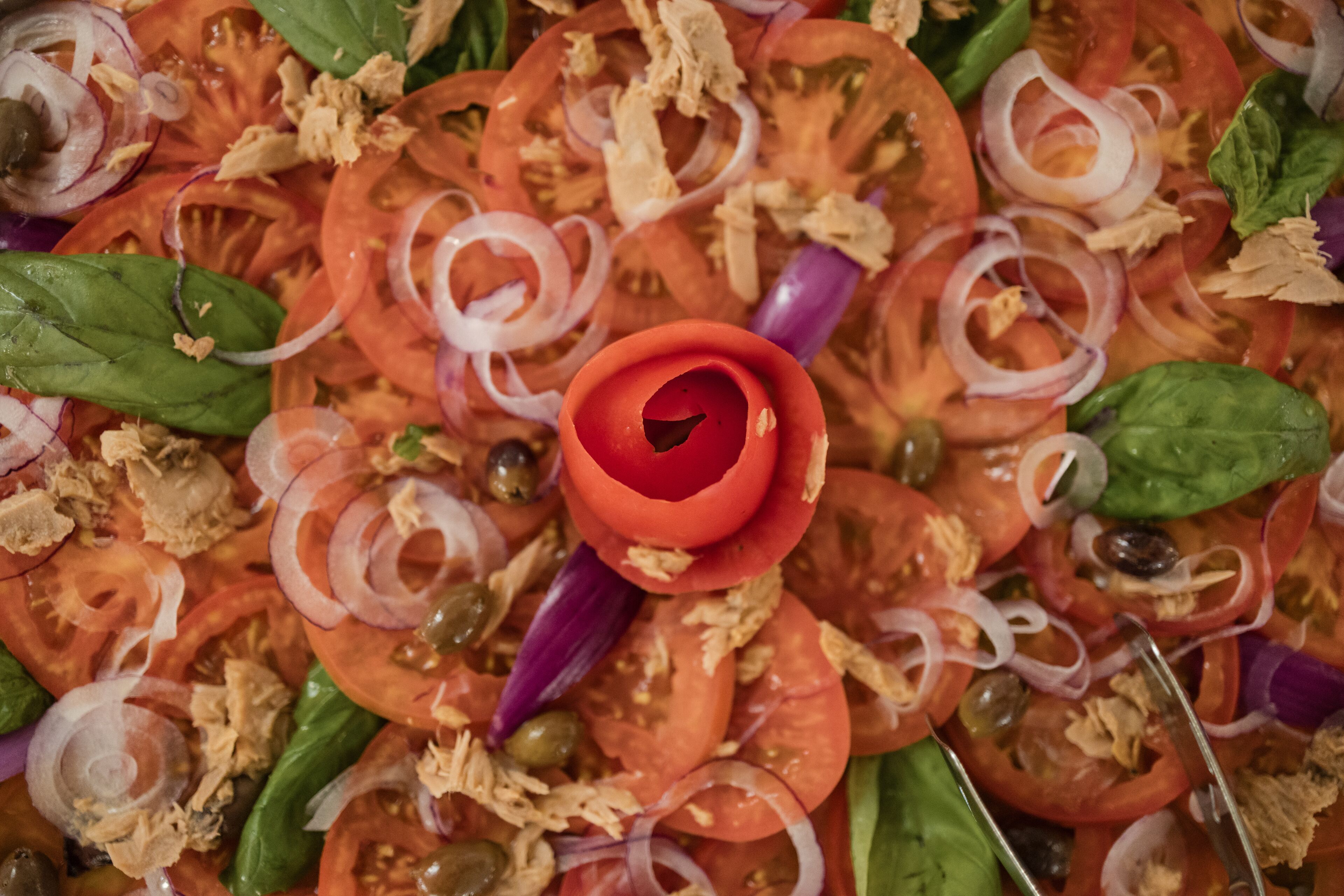 A salad with tomatoes, onions, spinach, and olives.