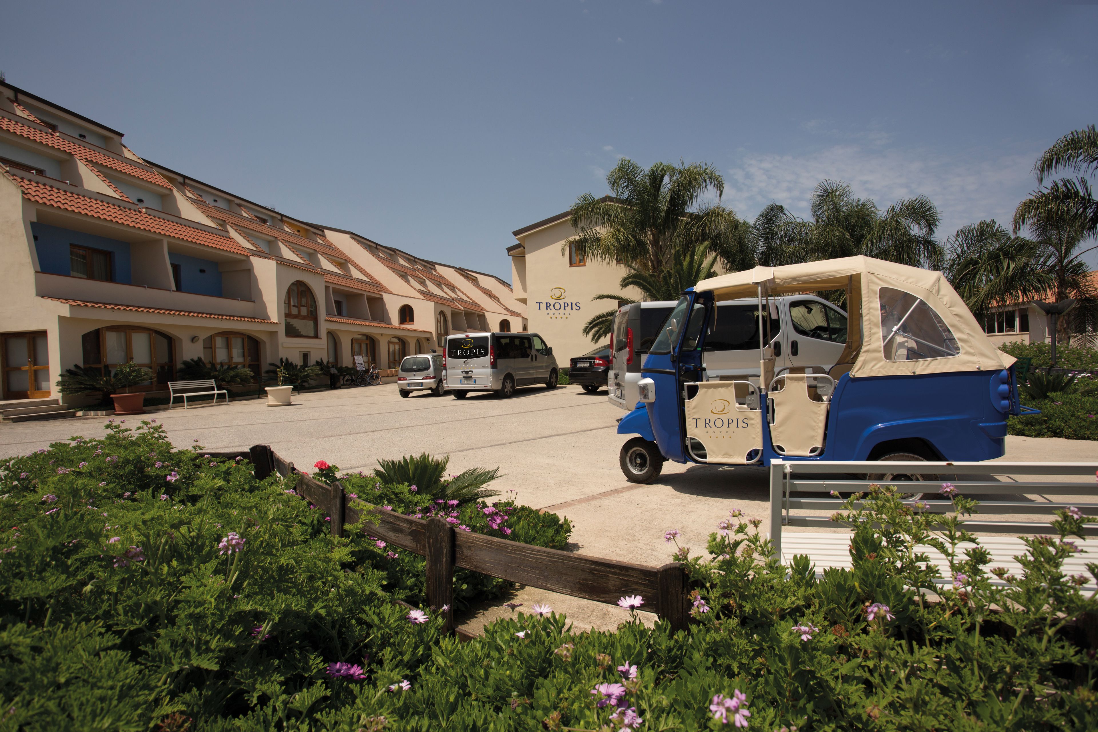 A building with a sign reading "TROPIS" and a blue and beige vehicle parked in front.