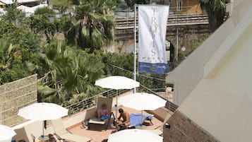 Ein Hoteldach mit mehreren Sonnenschirmen, einem Pool und Blick auf das Meer und die umliegenden Gebäude.