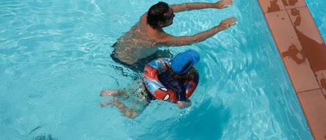 A swimming pool with clear blue water, a tiled edge, and a person in the water.