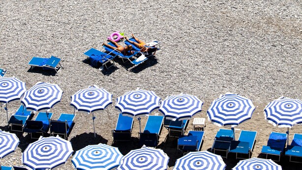 A beach with rows of blue lounge chairs and white and blue striped umbrellas. - Hotel Parigi & Spa (Bordighera)