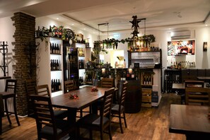 A restaurant with a brick column, wooden tables, and chairs. There are shelves with wine bottles and a bar area with a television. - Baden Hotel Bonn (Bonn)