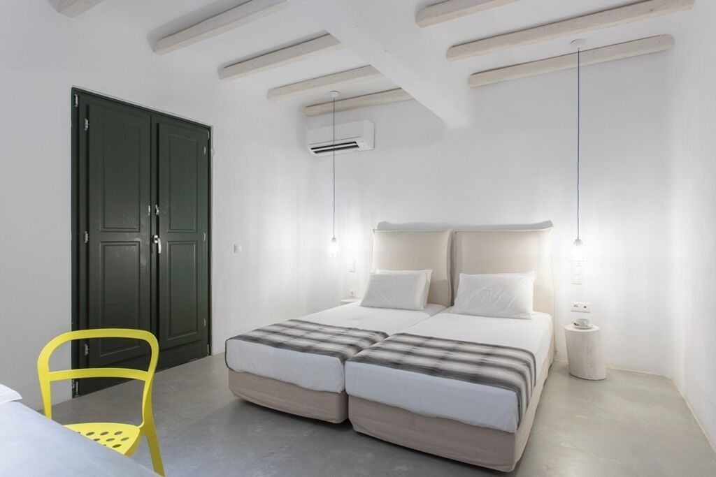 Een slaapkamer met een bed, nachtkastjes, een airconditioning en een stoel, plus een deur.