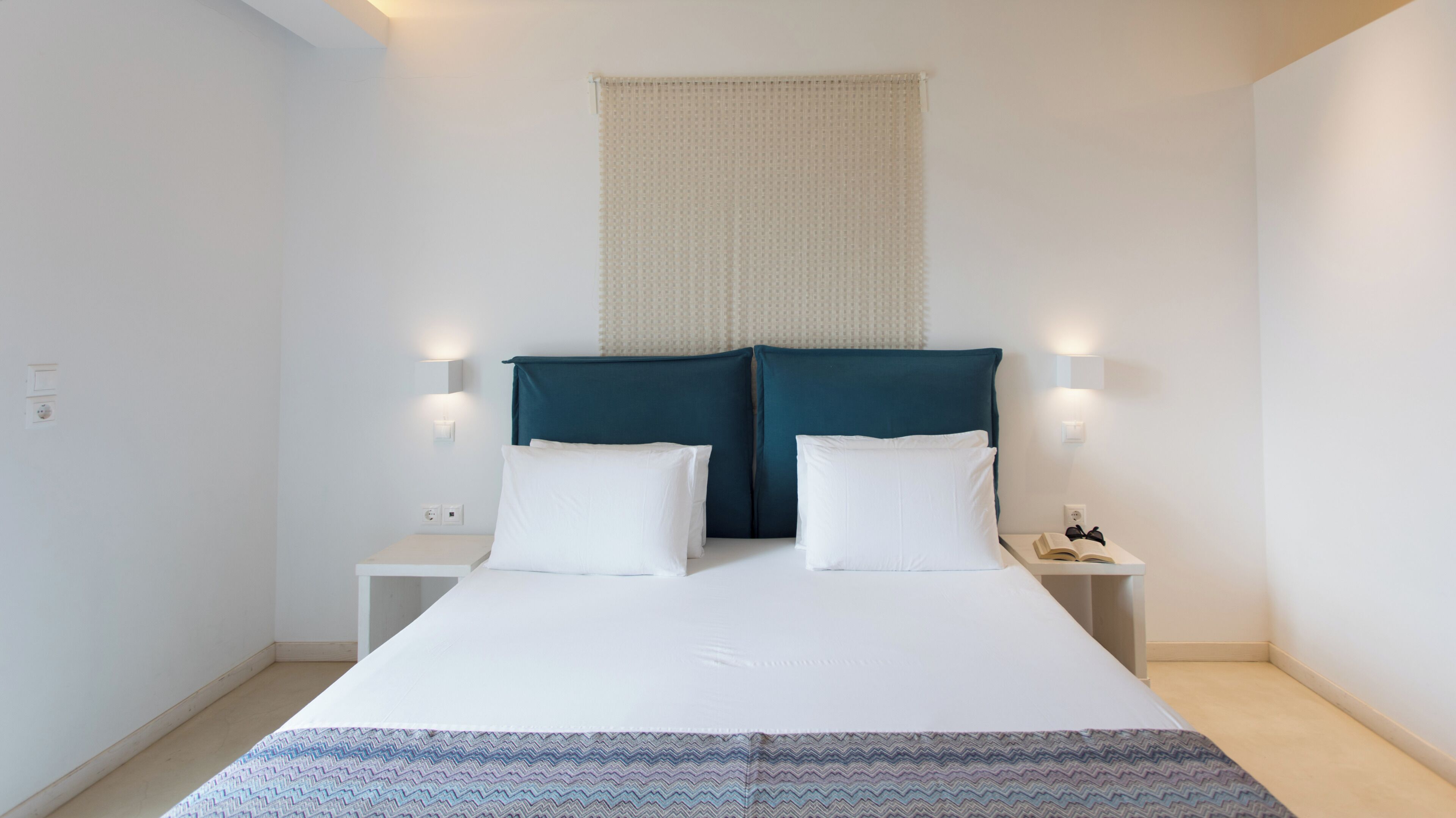 Een hotelkamer met een bed, twee nachtkastjes en een wandlamp.