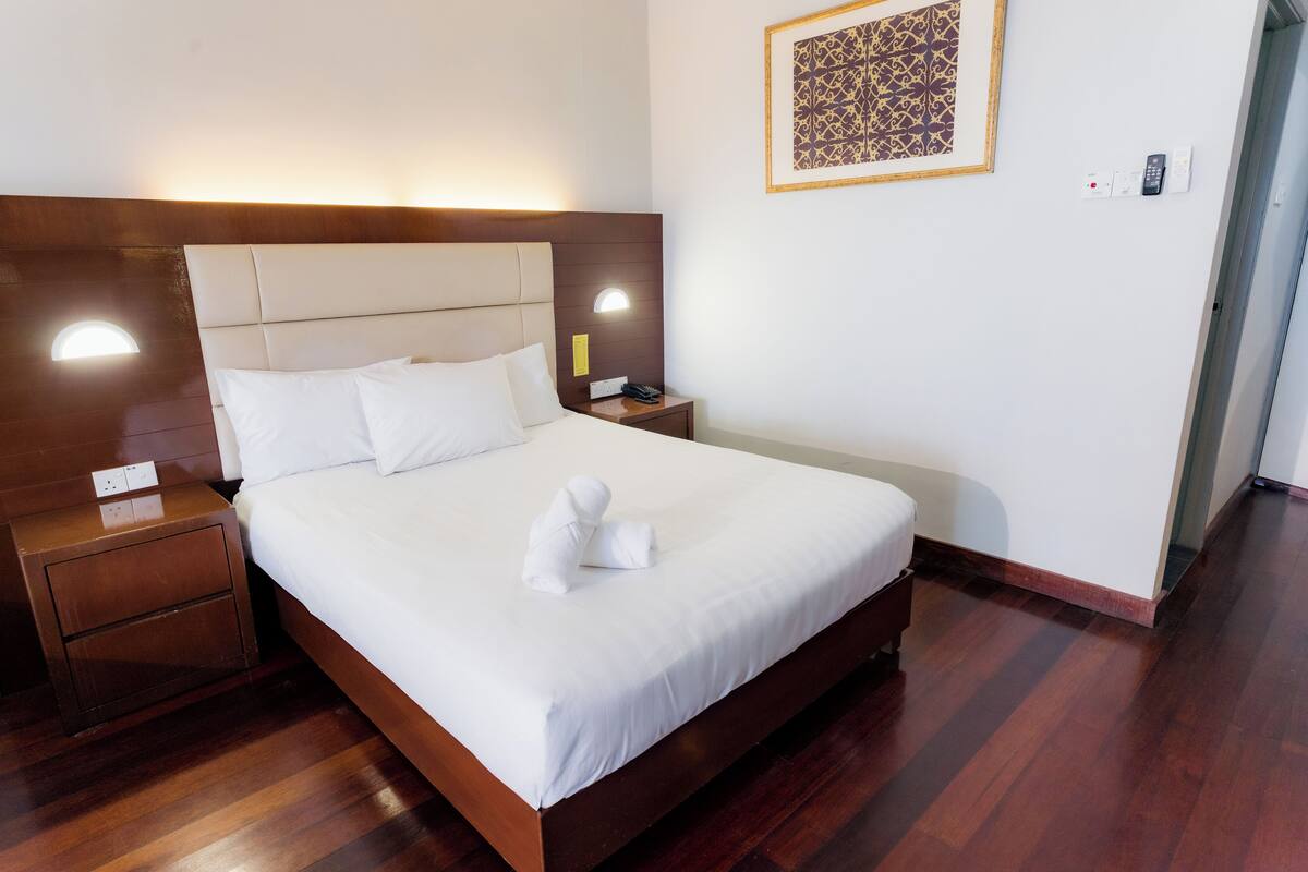 A neatly made bed with white linens, a wooden headboard, and a bedside table with a lamp.