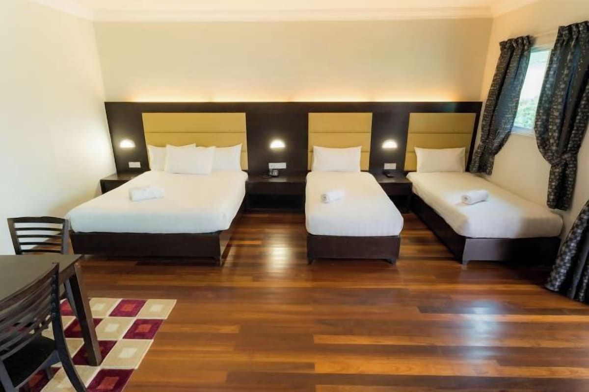 A hotel room with two beds, a wooden floor, a small table, and a chair.