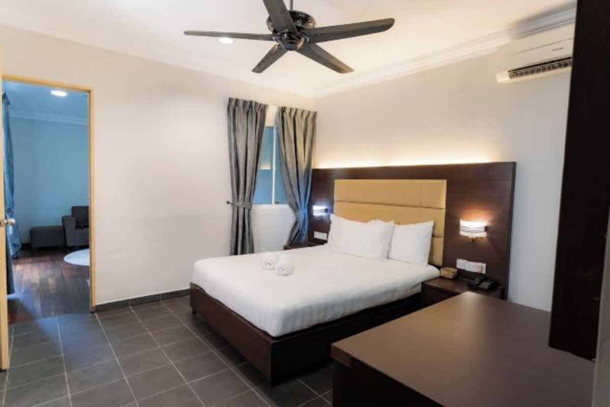 A hotel room with a bed, a desk, a ceiling fan, and an air conditioning unit.