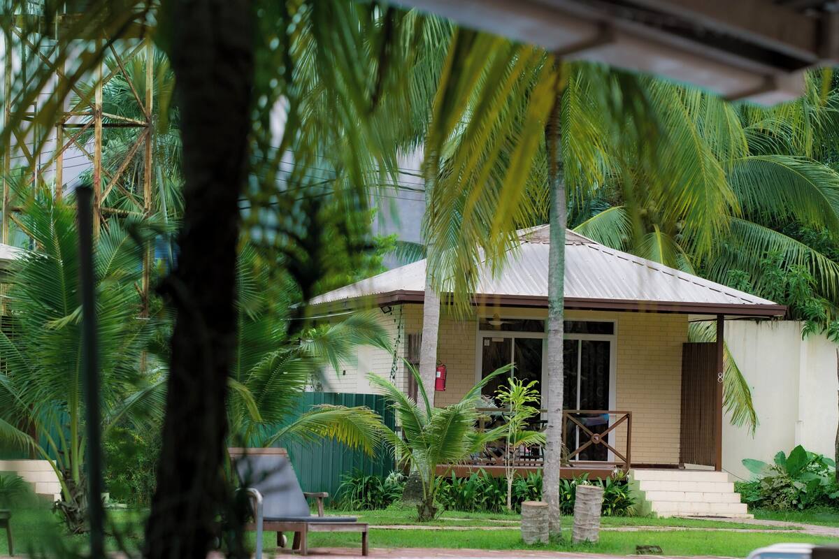 A poolside view of a house with a covered patio, surrounded by palm trees and greenery.