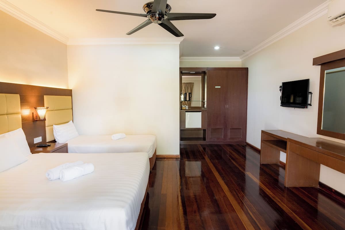 A hotel room with two beds, a ceiling fan, a TV, and a wooden desk.