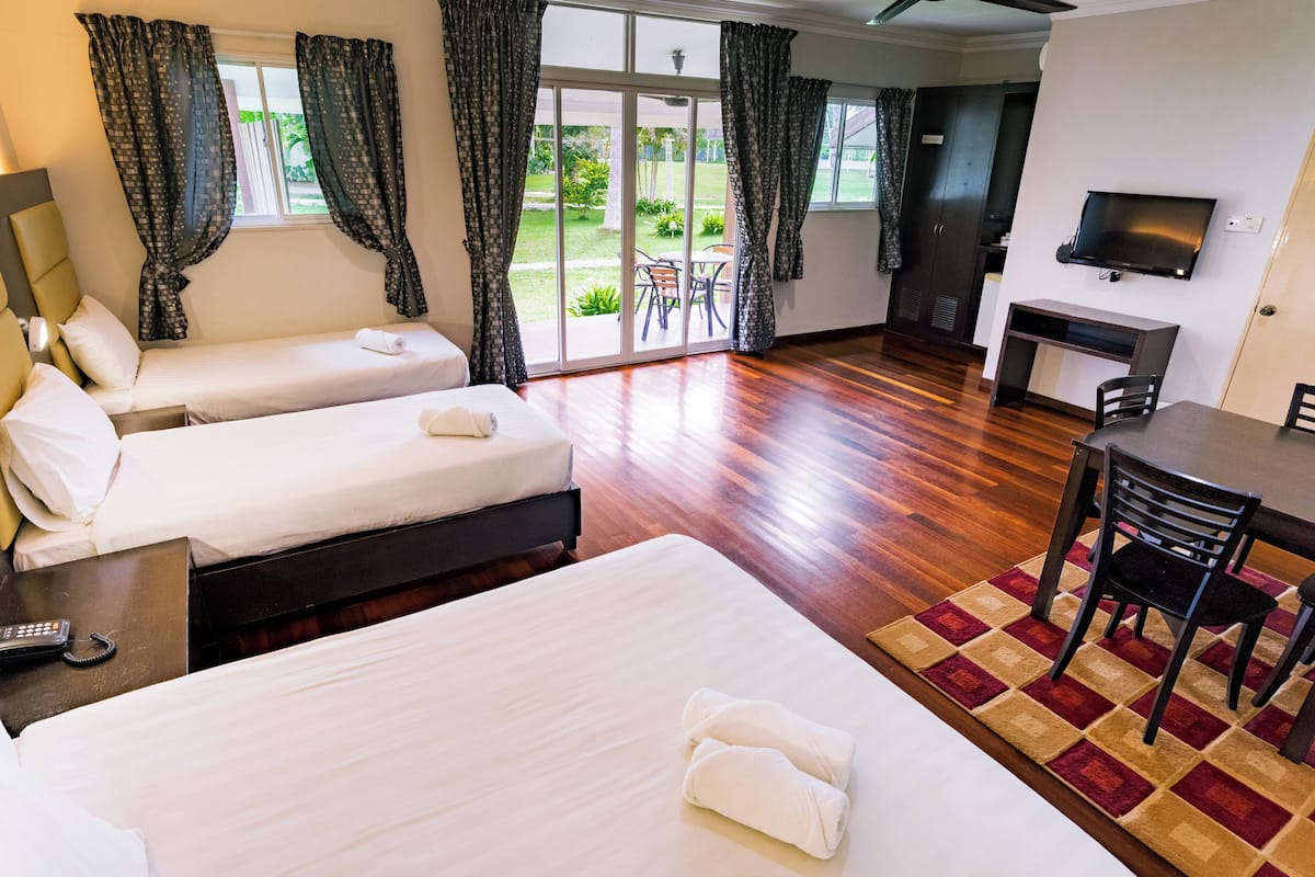 A hotel room with two beds, a TV, a desk, and a view of the garden.