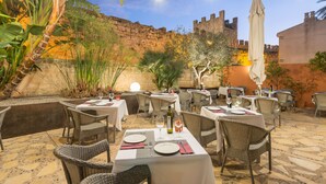 An outdoor dining area with tables and chairs, string lights, and a backdrop of a stone wall and greenery. - Can Simo Turismo de Interior (Alcúdia)