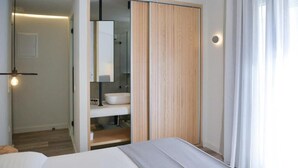 A modern bedroom with a bed, a wooden wardrobe, a bathroom with a sink and mirror, and a hanging light fixture.