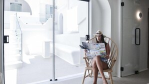 A person sitting on a wooden chair in a modern, well-lit room with a glass partition, reading a magazine.
