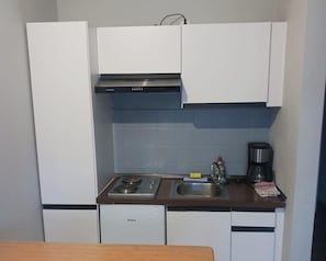 A compact kitchenette with a stove, sink, and coffee maker. - Pension Strohm im Lieth-Café (Bad Fallingbostel)