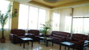 A spacious lobby with leather sofas and a coffee table, large windows with curtains, and a potted plant. - Ancor Hotel (Voluntari)
