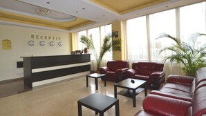 A reception area with a black reception desk, red leather sofas, and two small tables. - Ancor Hotel (Voluntari)