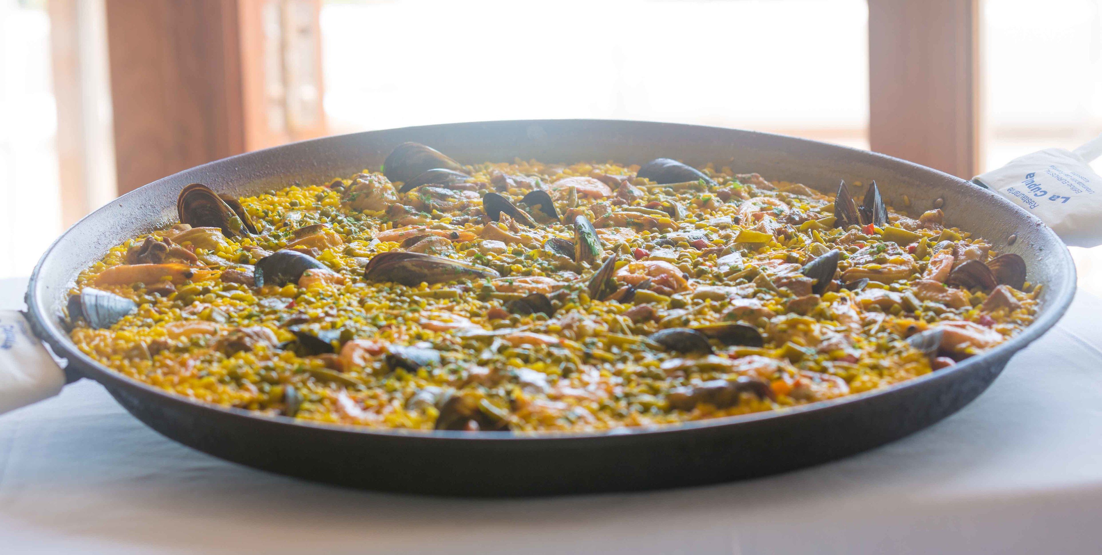 Una paellera grande, redonda y poco profunda, llena de una paella de mariscos colorida.