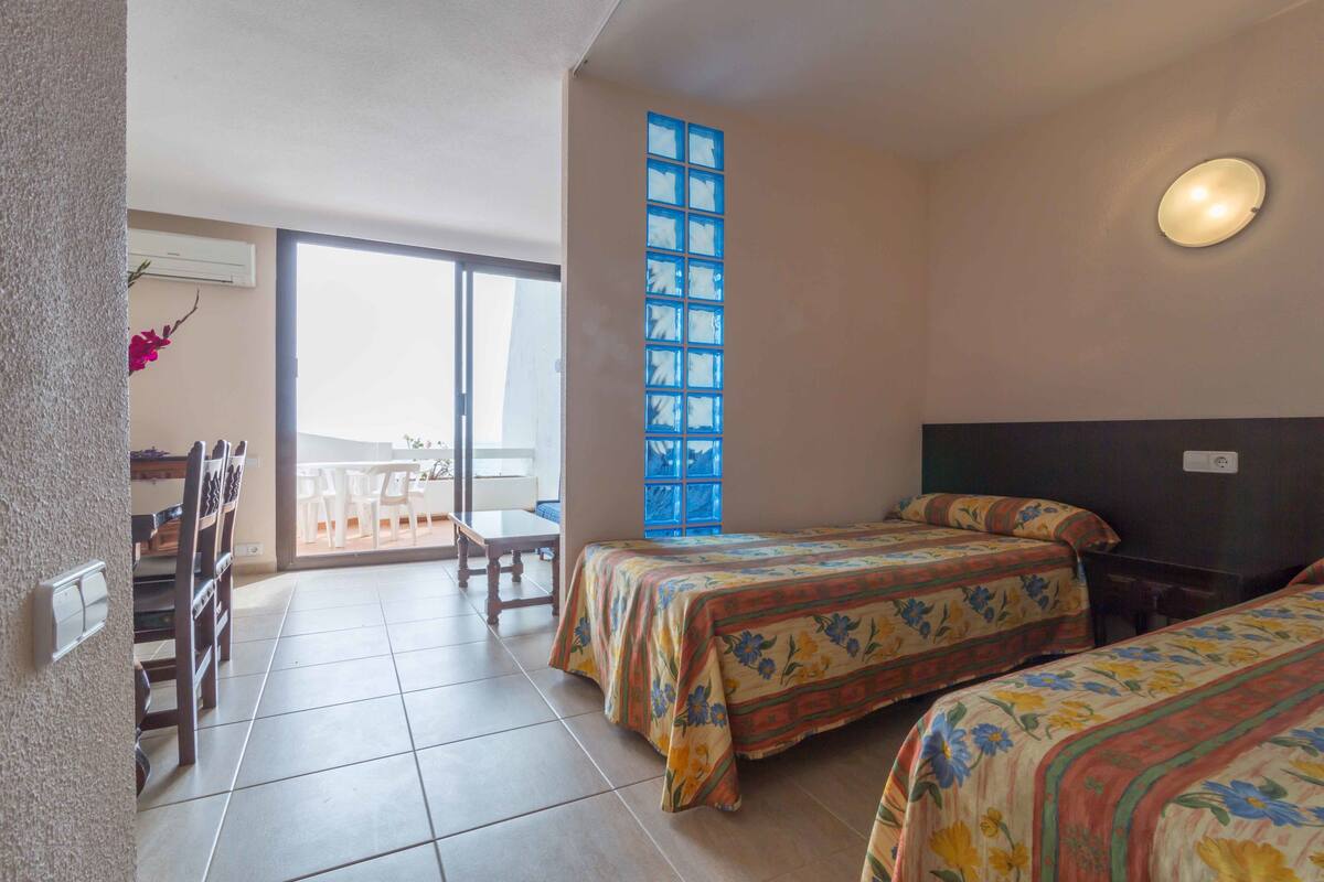 A hotel room with two beds, a balcony, a large window, and a ceiling light.