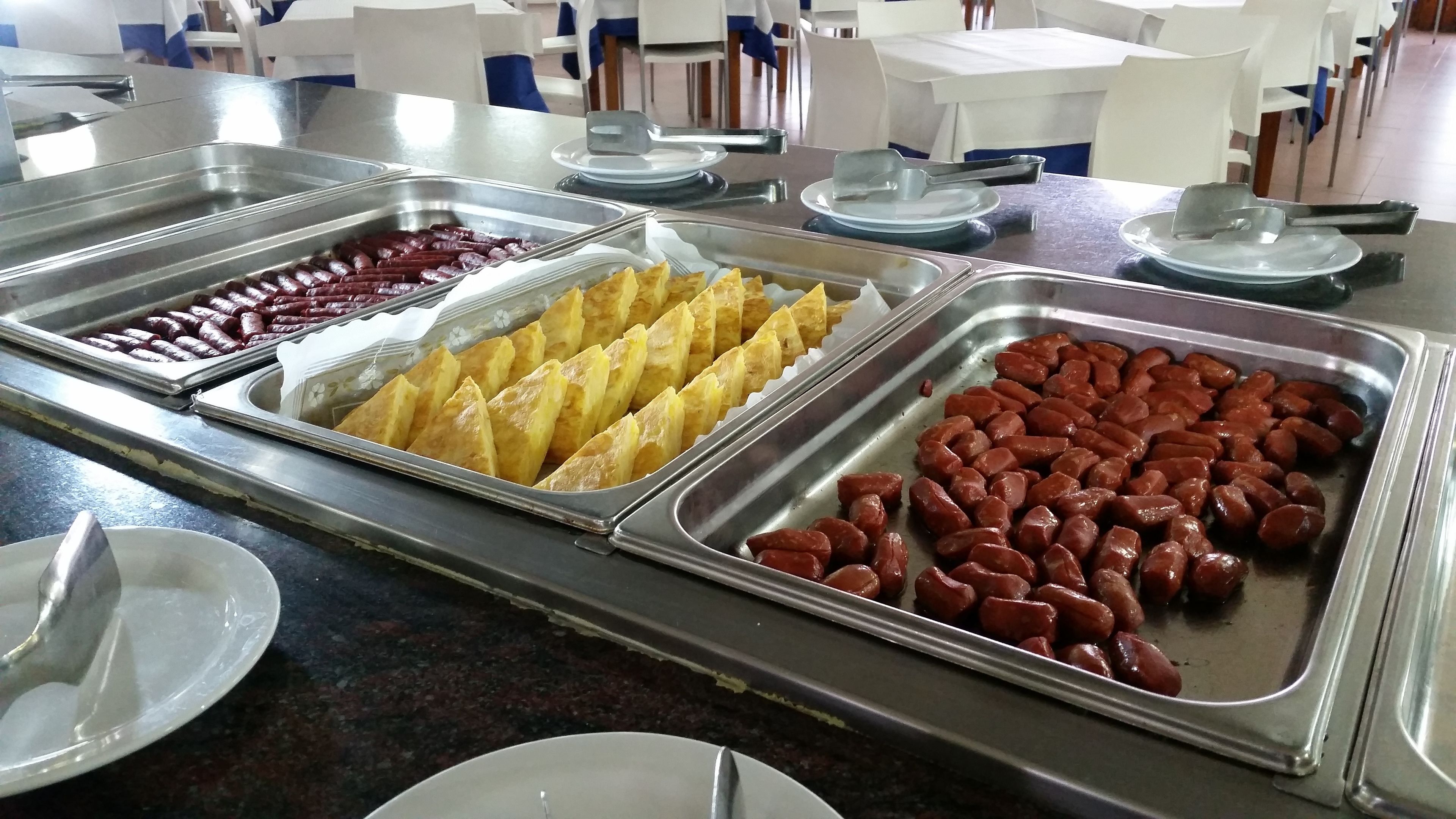Un bufé con diversos alimentos, incluyendo salchichas, bollería y otros platos.